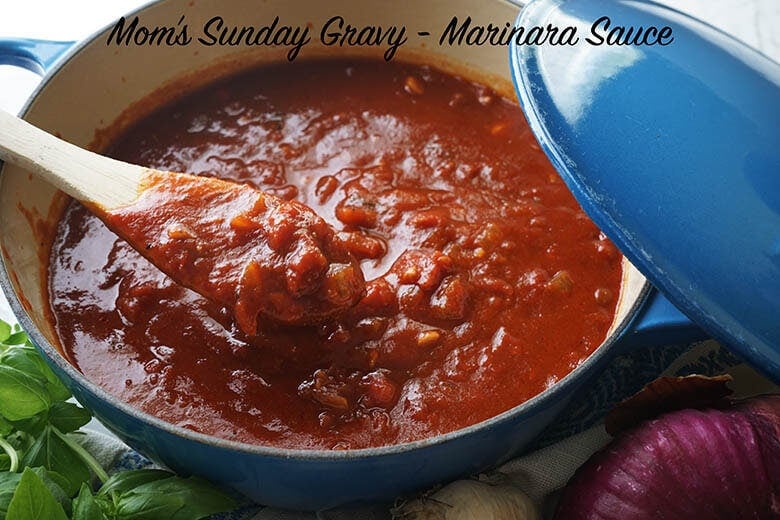Recipe for marinara sauce simmering in a blue pot surrounded by fresh basil and onions.