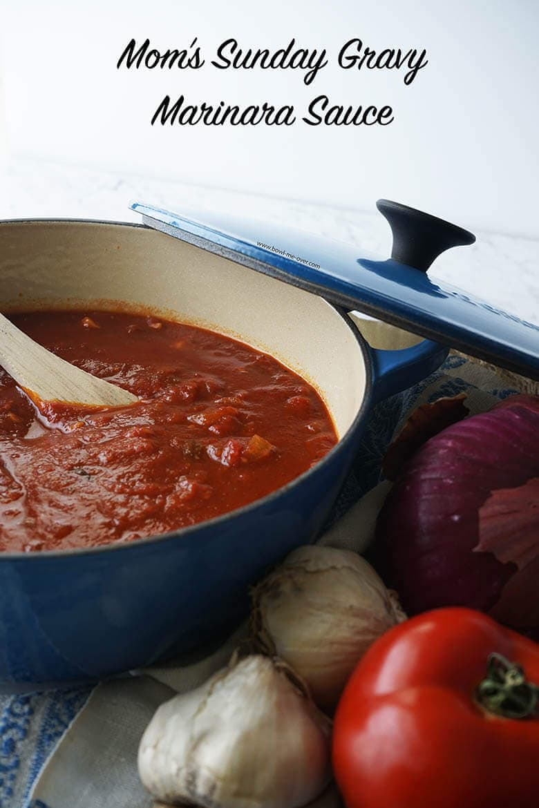 Marina recipe in a blue pot surrounded by fresh garlic, tomatoes and onions.