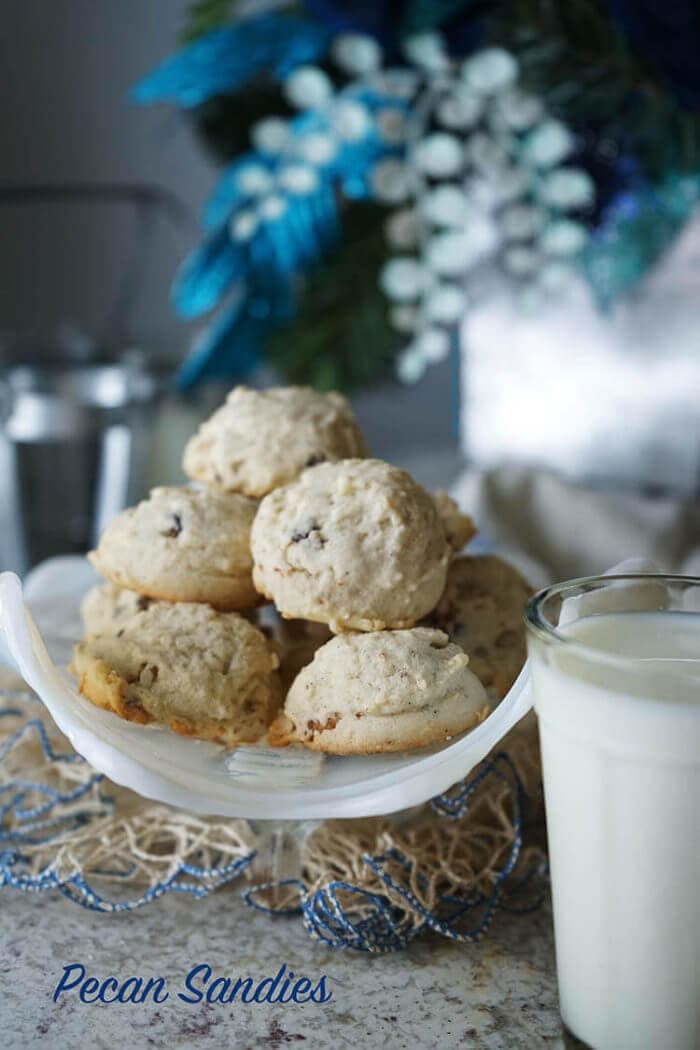 A white bowl full of Homemade Pecan Sandies with a glass of milk ready to dunk cookies into. This pecan sandies recipe was my Grandma's and these cookies are delicious!
