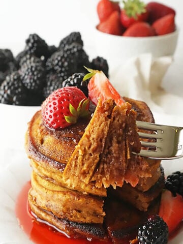 Stack of pumpkin pancakes on plate with strawberries.