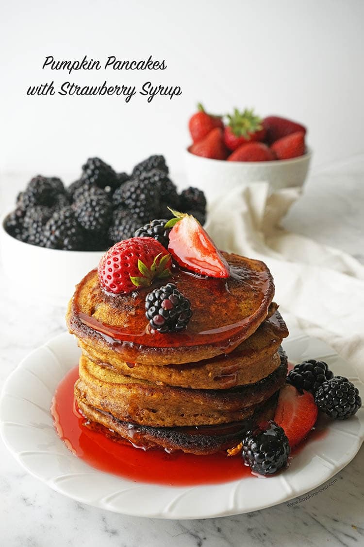 Stack of flapjacks on plate drizzled with syrup and topped with fruit.