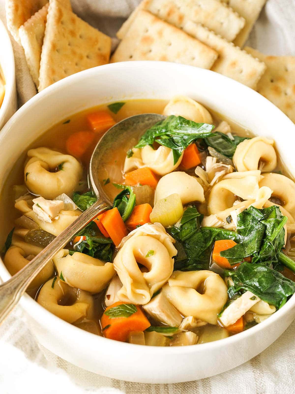 Chicken Tortellini Soup with Spinach in bowl with crackers.