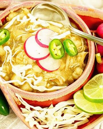 Verde chicken posole in a bowl topped with cabbage, radishes and jalapeños.