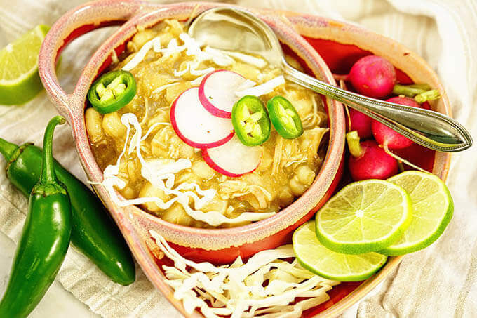 Verde chicken posole in a bowl topped with cabbage, radishes and jalapeños.