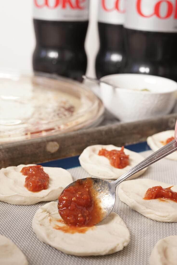 Spoon adding sauce to the middle of a small piece of pizza dough. 