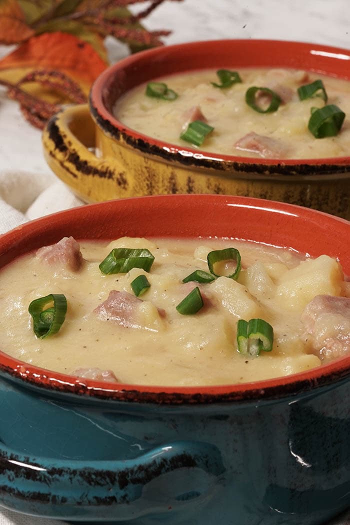 Two big hearty bowls of potato soup with ham topped with thinly sliced green onions.