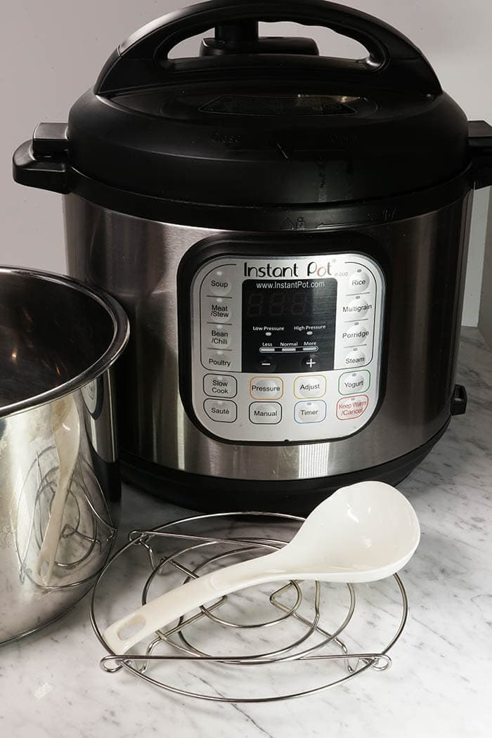 An Instant Pot Pressure Cooker equipped with a stainless steel pot, small white ladle and steaming rack.
