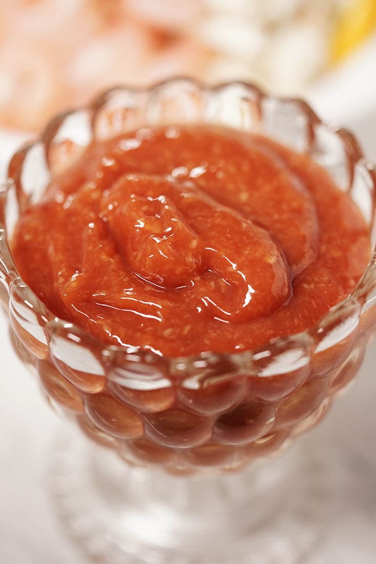 A close up view of a glass bowl full of spicy and tangy shrimp cocktail sauce recipe.