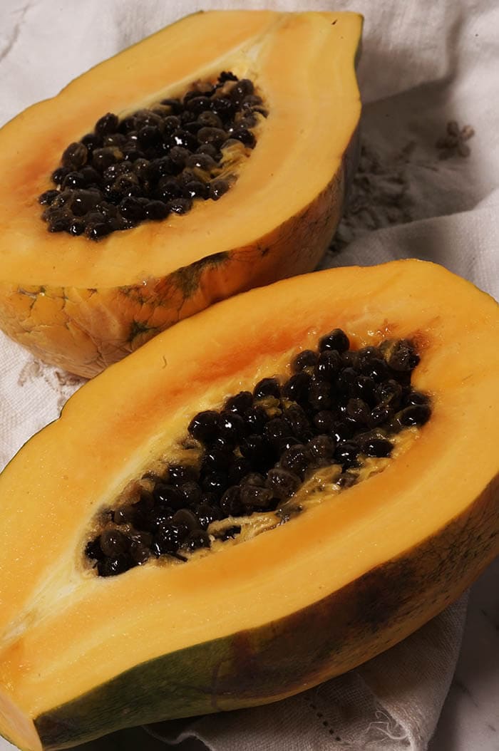 A picture of bright orange papaya sliced open showing the bright orange flesh and black seeds.