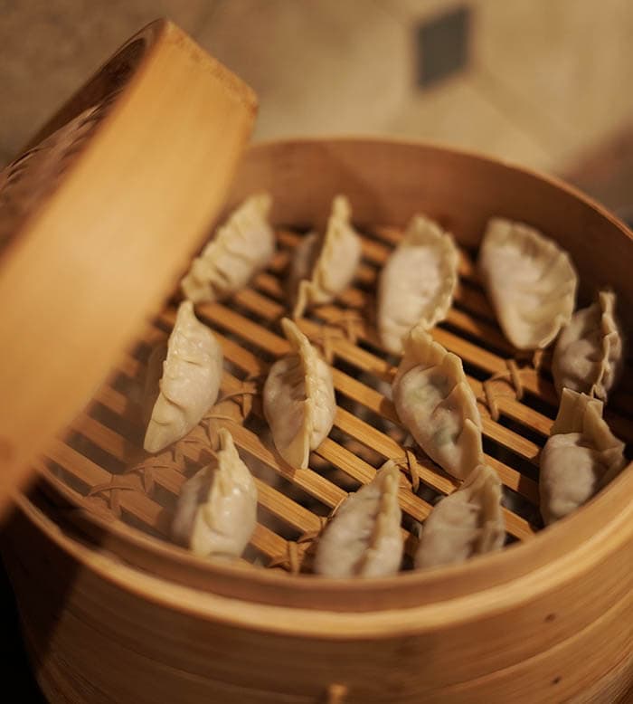 A bamboo steamer filled with pot stickers steaming on the stove
