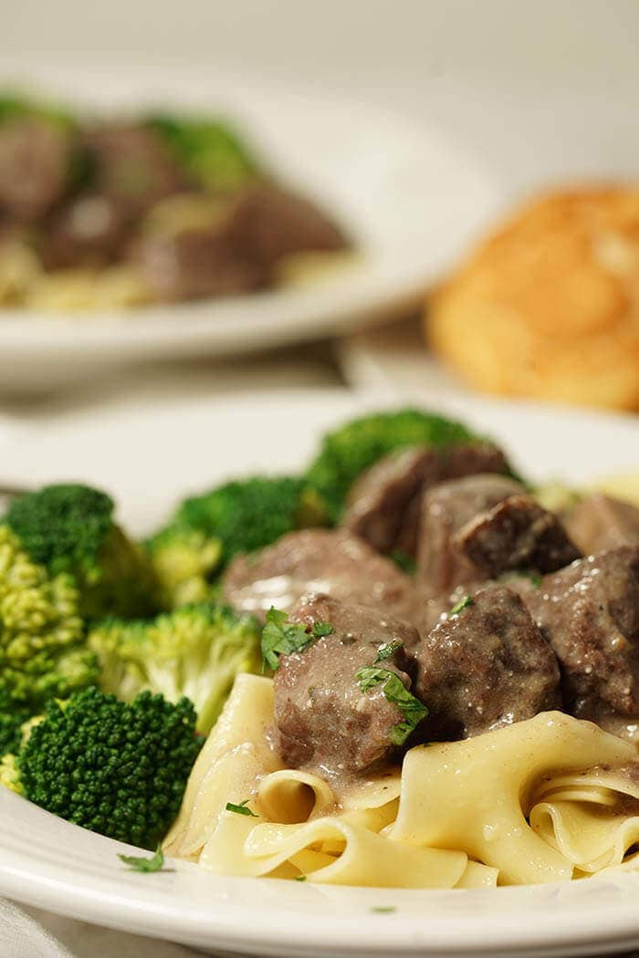 A delicious comforting serving of beef tips ladled over egg noodles served up with steamed broccoli and a roll.