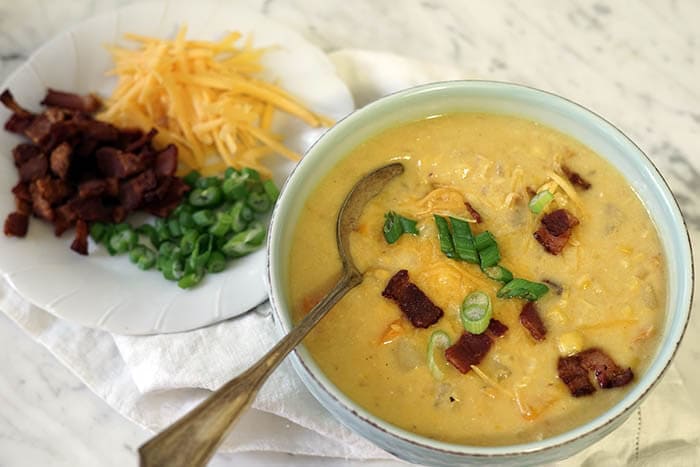 A green bowl of corn and potato chowder garnished with bacon, sliced green onions and cheese.