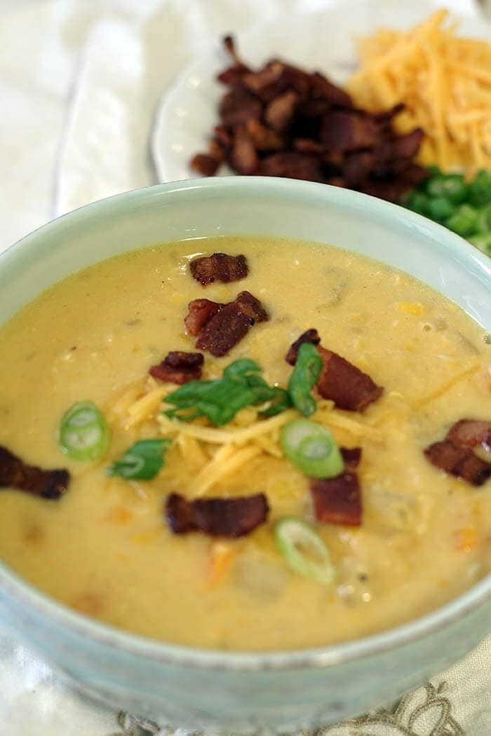 A green bowl full of corn and potato chowder. The chowder is topped with crispy bacon, sliced green onions and a big of shredded cheddar cheese.