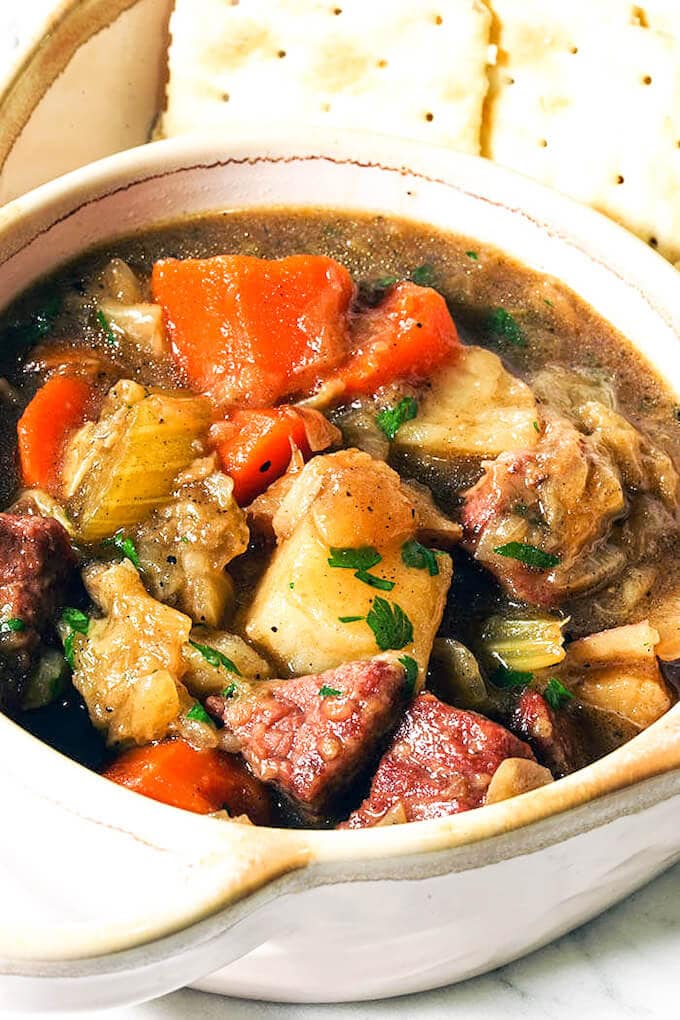 Sopa de carne en conserva y repollo en un tazón blanco con una porción de galletas saladas.