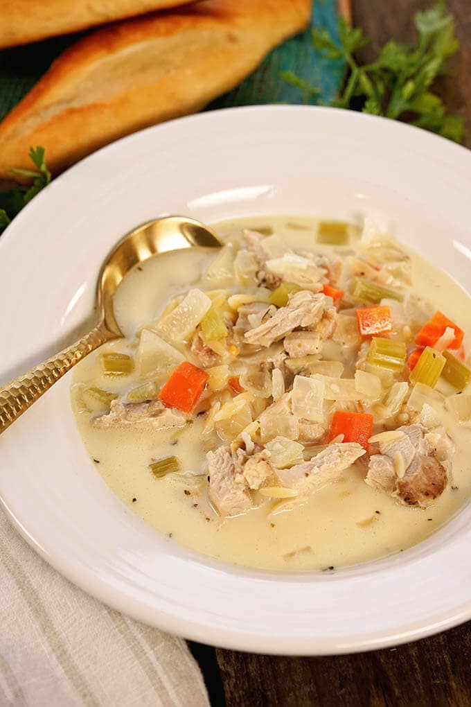 A white bowl filled with Copycat Panera Lemon Chicken Soup. With a soup spoon.