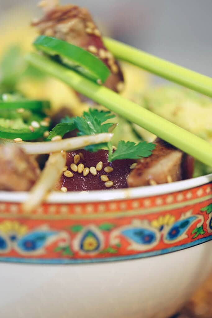 A bowl of seared tuna poke. A pair of green chopsticks grabs some tuna and is ready to take a bite!