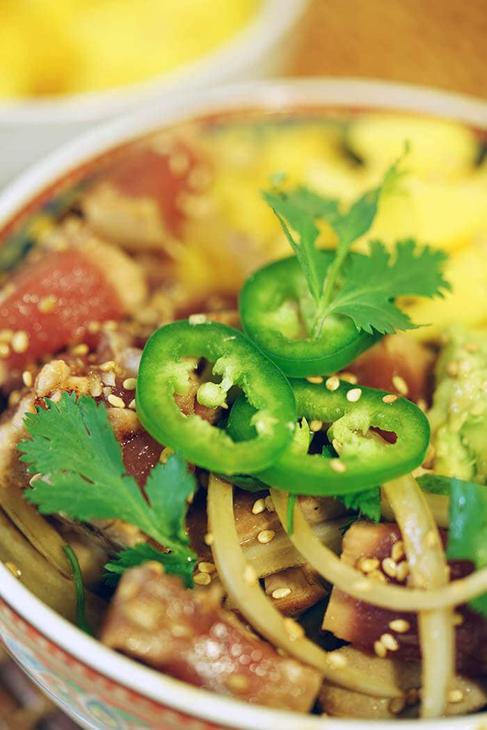 Bowl topped with with seared tuna, mango, avocado topped with sliced jalapeños and cilantro.