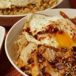 A close up of a Korean Rice Bowl with kimchi, grilled chicken marinated with a Korean BBQ Sauce Recipe and topped with a runny egg.