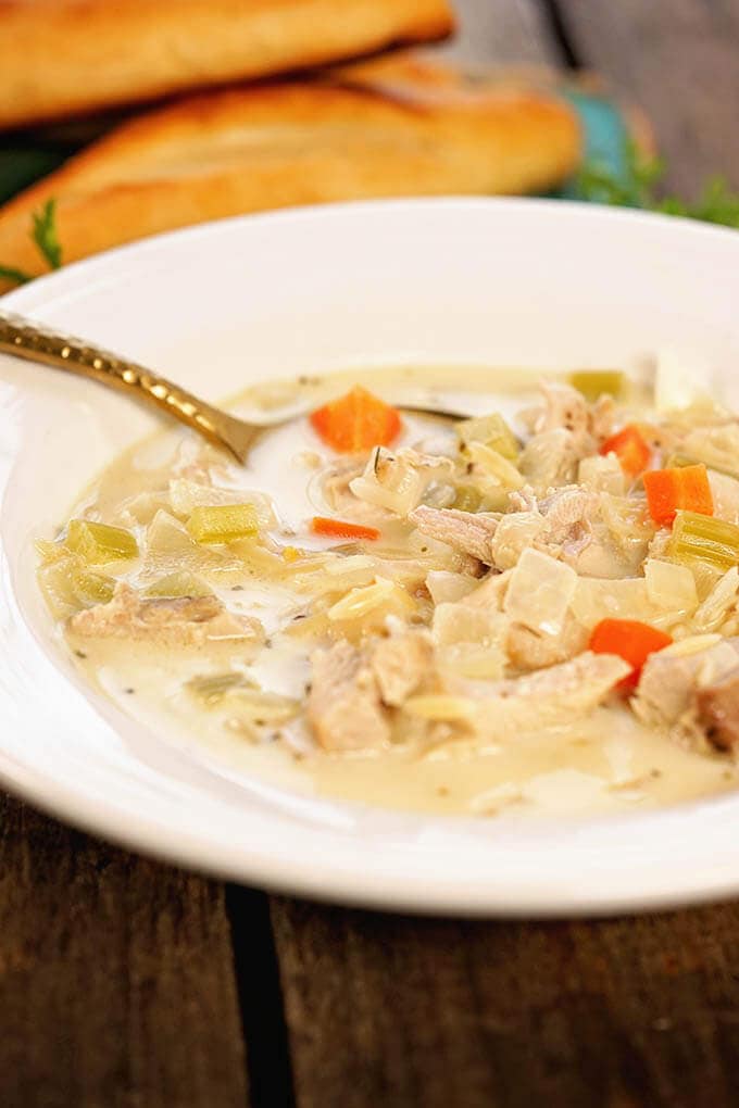 A white bowl filled with Copycat Panera Lemon Chicken Soup with breadsticks.