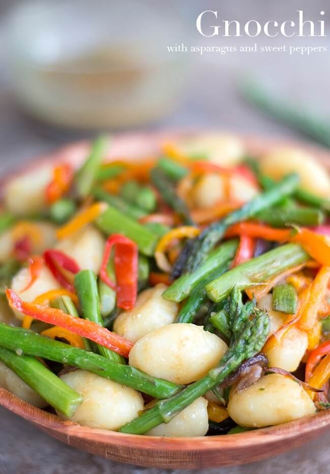 A bowl full of gnocchi pasta, sweet asparagus with red and orange bell peppers. This is a bright fresh vegan meal.