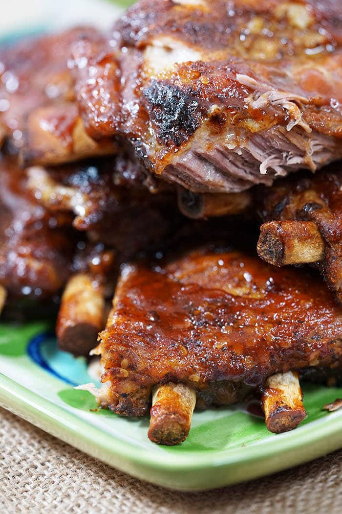 A green platter piled high with Barbecue Pork Ribs that have been slathered in bbq sauce.