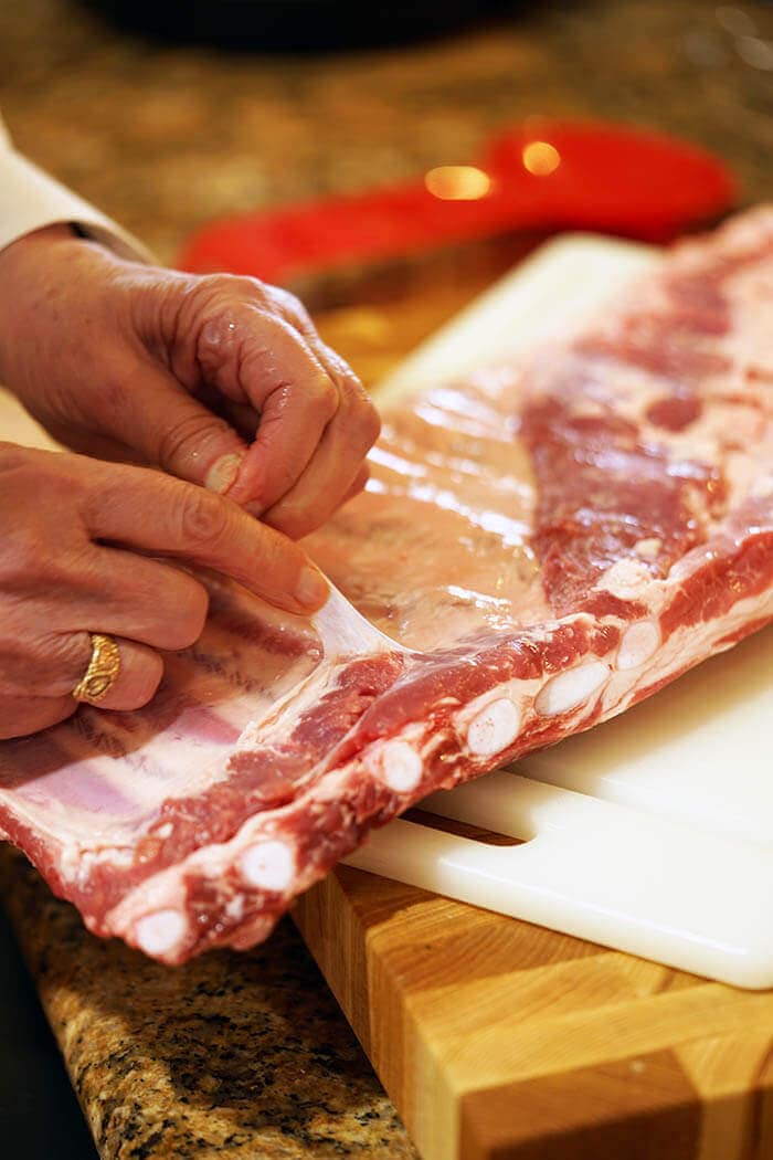 A slab of pork ribs being prepped for cooking. The chef is peeling the silver skin off the back of the ribs.