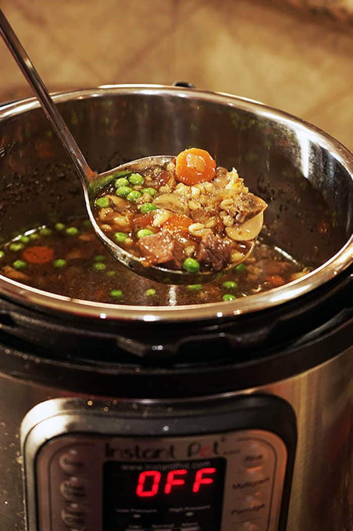 A ladle of beef barley soup being scooped out of an Instant Pot.