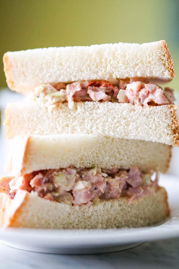 A sandwich made with ham spread on white bread. The sandwich is sliced in half and stacked up.