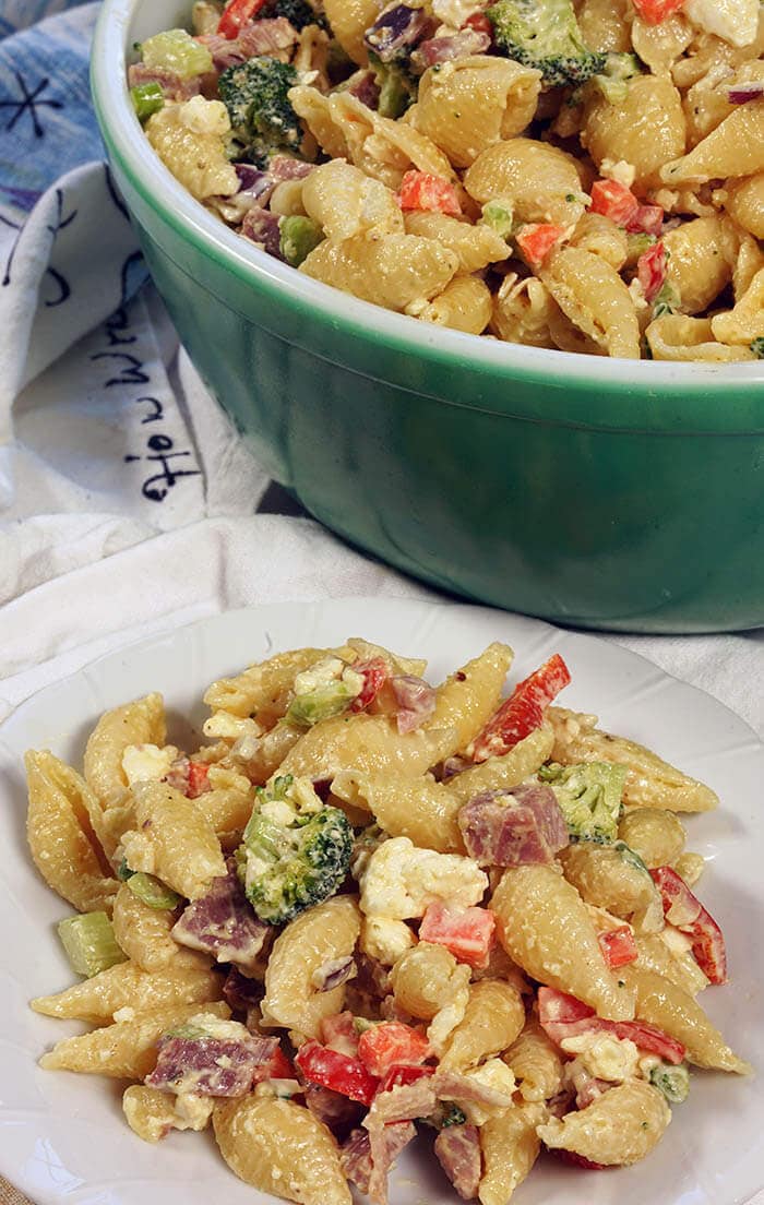 A large green bowl filled with pasta salad with ham. There's a white plate dished up and ready to be devoured!