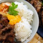 Korean BBQ Beef Bowl with beef, rice and kimchi., garnished with sliced mandarins.