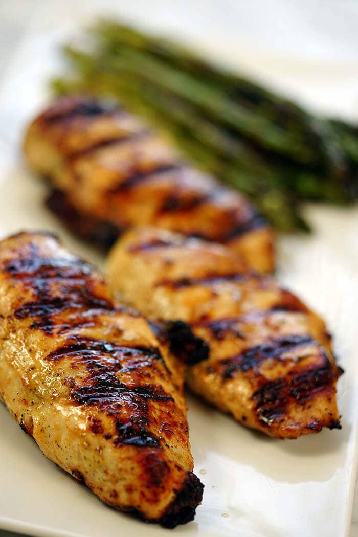 Lemon pepper marinade grilled chicken breasts on a white plate with some grilled asparagus.