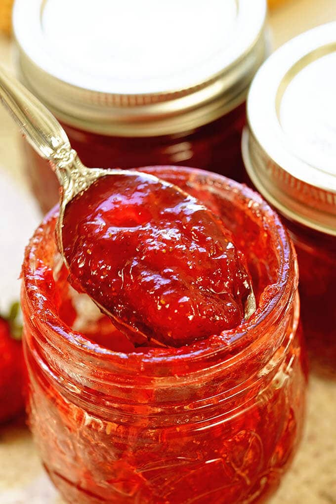 A jar of strawberry jam with a spoon dishing out the bottom of the jar!