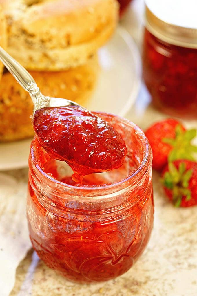 A jar of strawberry jam and bagels.
