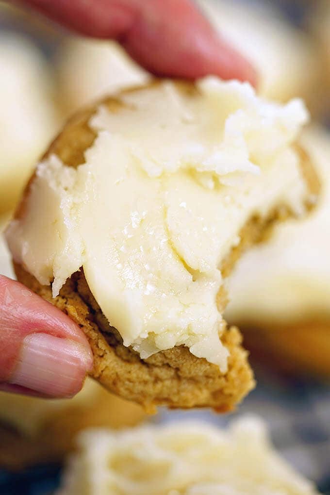 Hand holding a frosted cookie and a bite has been taken from the cookie.