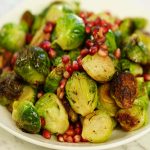 Brussels Sprouts in white bowl topped with pomegranate seeds.