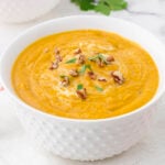 White bowl filled with Autumn Squash Soup topped with chopped nuts.