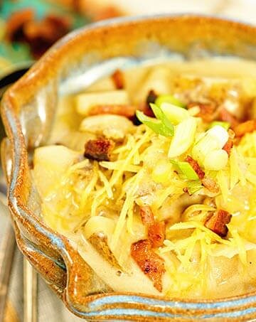 Loaded Potato Soup Recipe topped with cheese, onions and bacon in a blue bowl on a white counter.