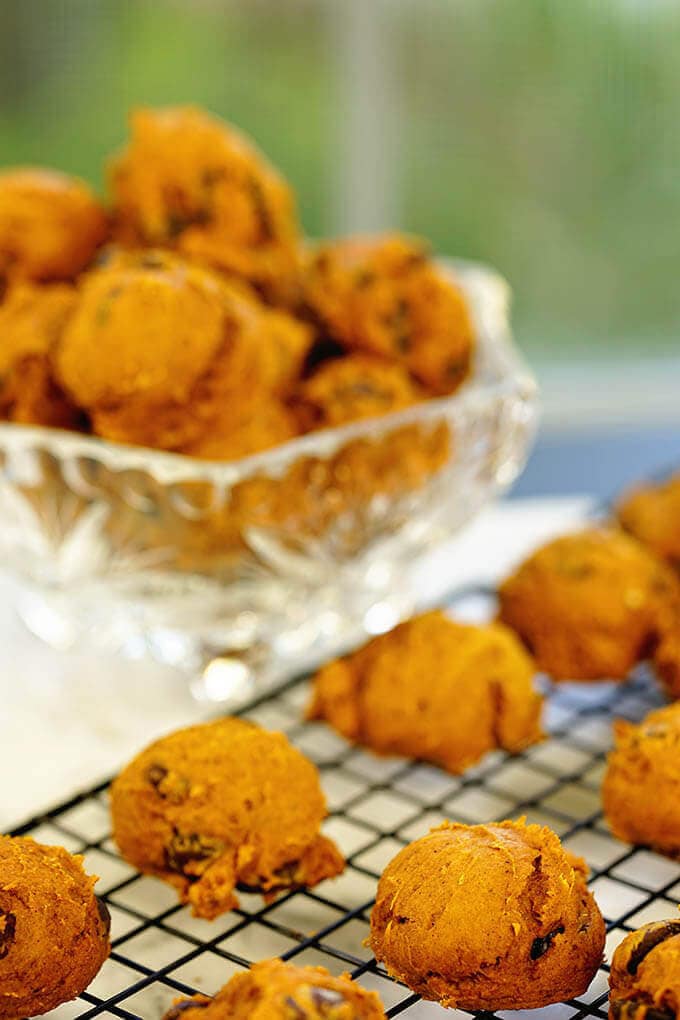 The Best Pumpkin Cookies on a cooling rack with a glass bowl filled with cookies in the background.