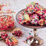 Homemade Shortbread cookies on a silver platter on a marble board surround by piles of sprinkles!