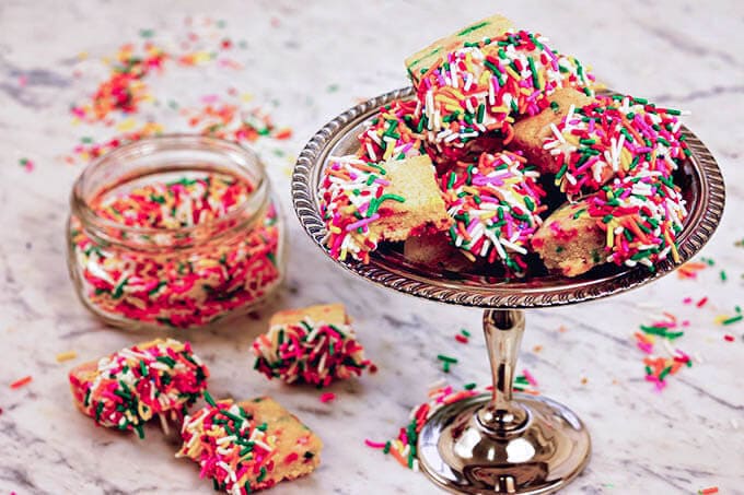 Homemade Shortbread cookies on a silver platter on a marble board surround by piles of sprinkles!