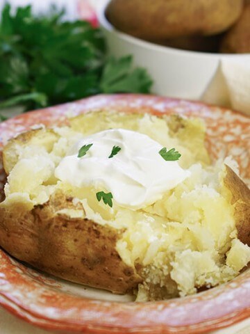 Instant Pot baked potatoes in a bowl topped with butter, sour cream and chives.