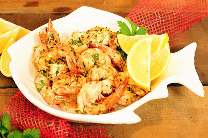 Garlic shrimp in a white bowl with wedges of lemon.