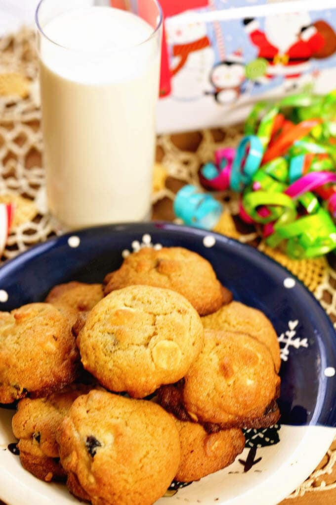 A blue plate filled with White Choc Macadamia Nut Cookies and a glass of milk