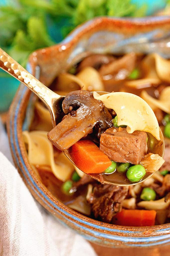 A spoonful of beef noodle soup with mushrooms, carrots, beef, green peas and noodles.