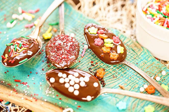 A blue platter with four chocolate covered spoons. Each spoon is topped with sprinkles.