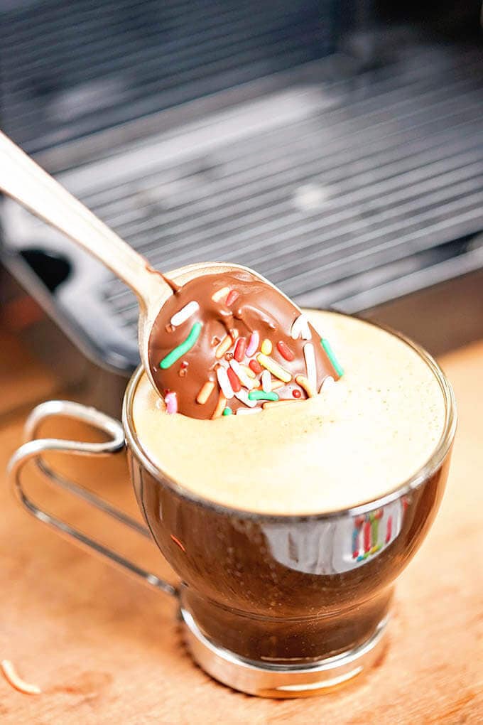 A chocolate covered spoon being stirred into espresso.
