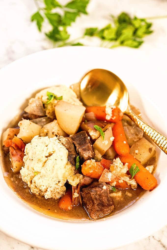 Beef stew with dumplings in a white bowl with spoon.