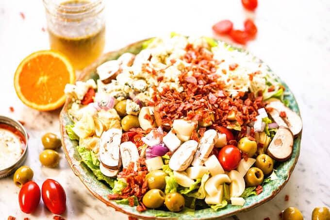 Best green salad in a bowl topped with all the fixings - olives, artichokes, cheese, tomatoes and onions with homemade vinaigrette.