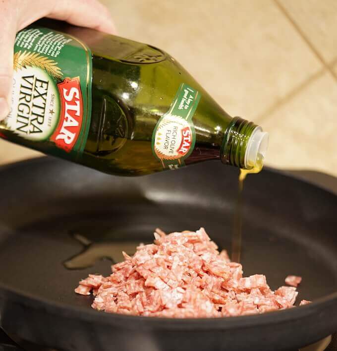 Minced salami in a cast iron pan. It is being fried with Extra Virgin Olive Oil