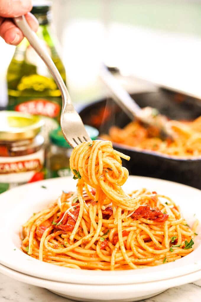 Pasta Puttanesca in white bowl with spaghetti twirled around fork..